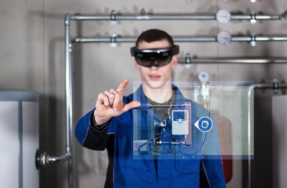 Facharbeiter Heizungsmonteur eine AR Brille aufgesetzt und schaut auf den Leser. Man erkennt die von der AR Brille eingeblendeten Informationen.